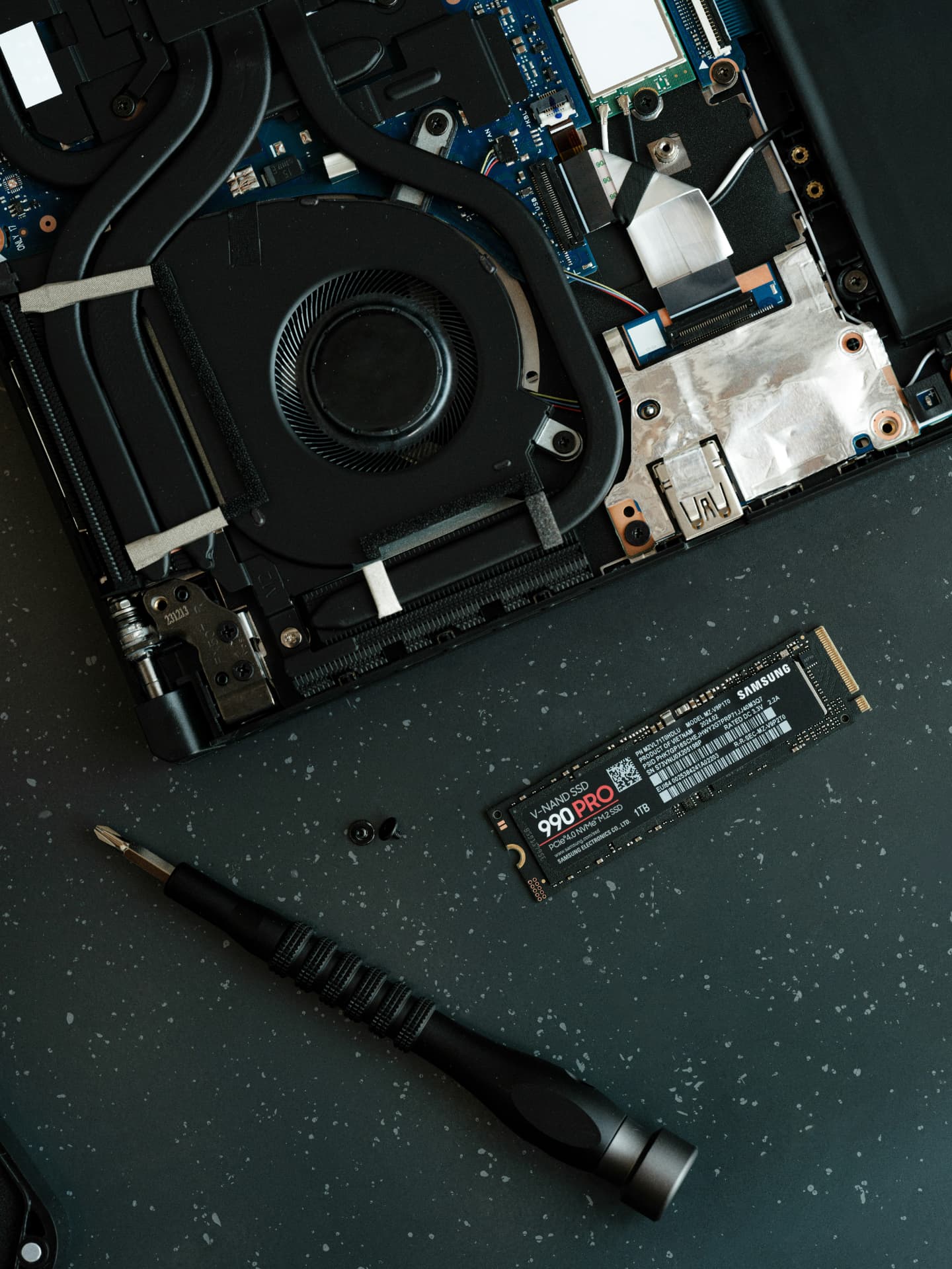 Open laptop beside a Samsung solid-state drive and precision screwdriver