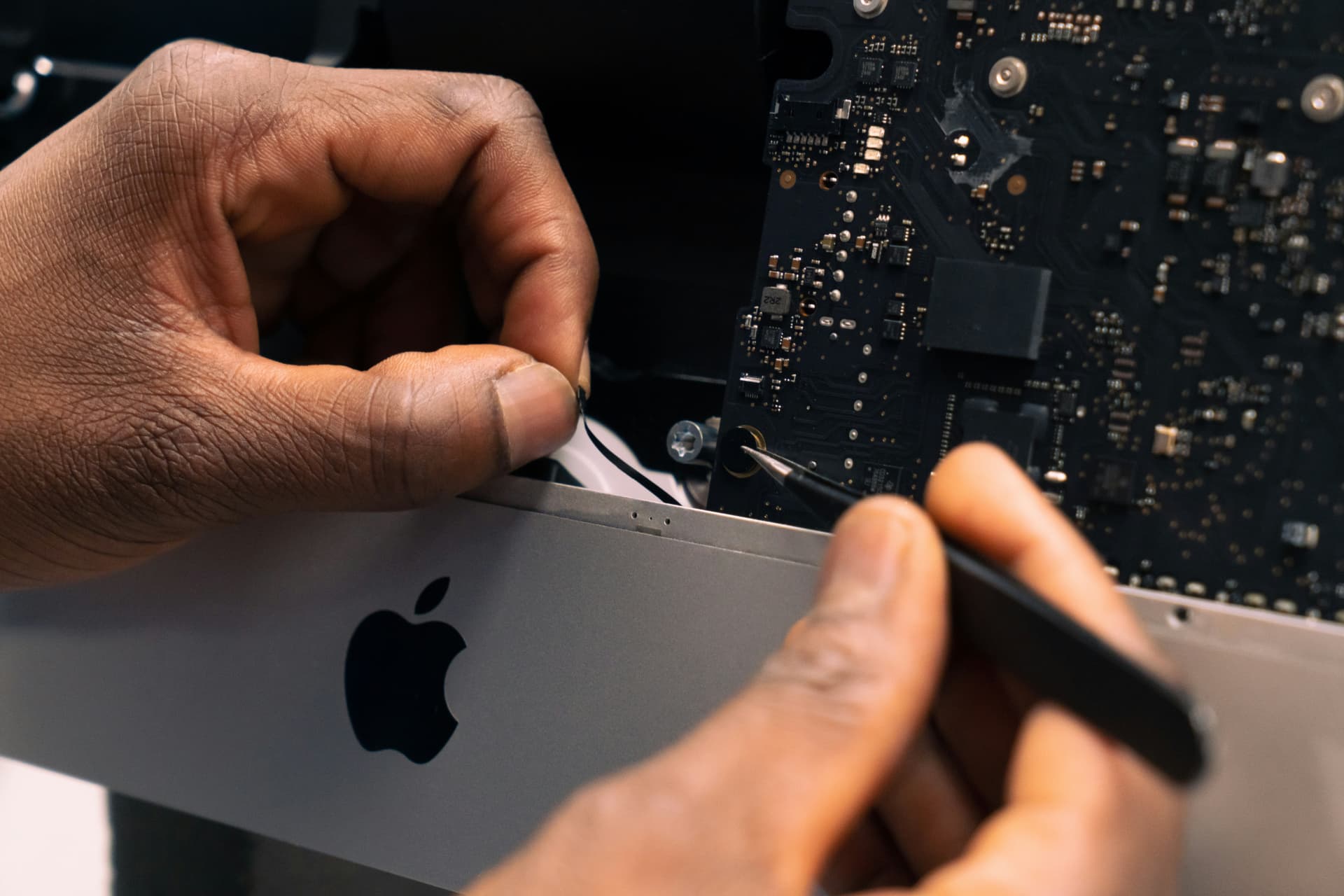 Technician inspecting a MacBook logic board with precision tools