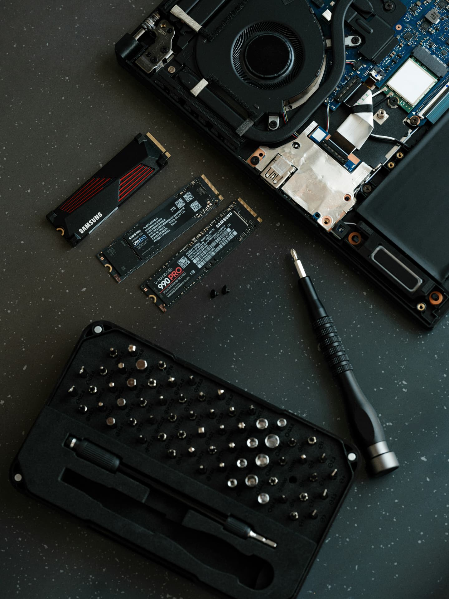 Laptop repair tools and solid-state drives arranged beside an open computer